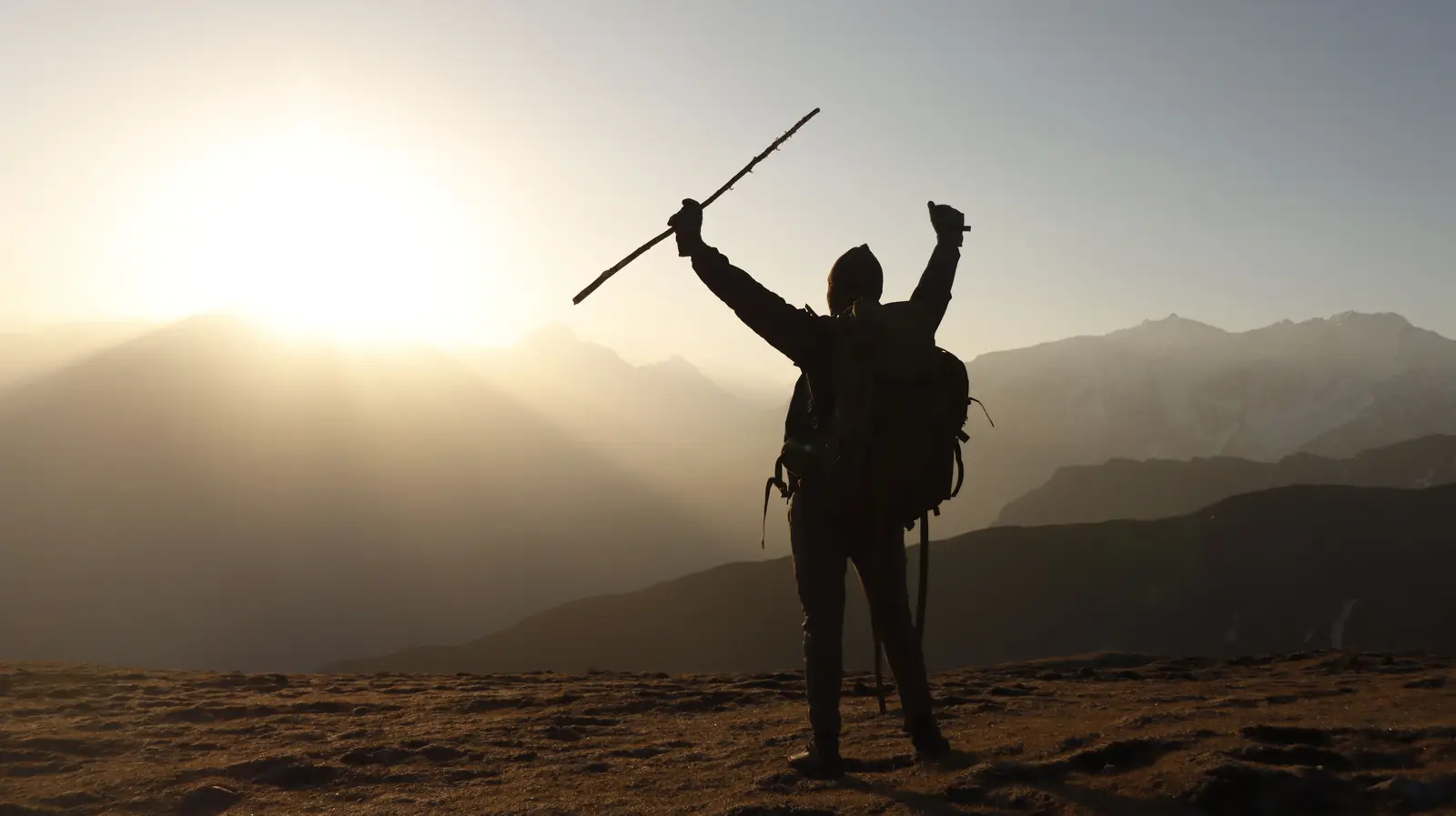 A hiker raising his walking stick after reaching the summit