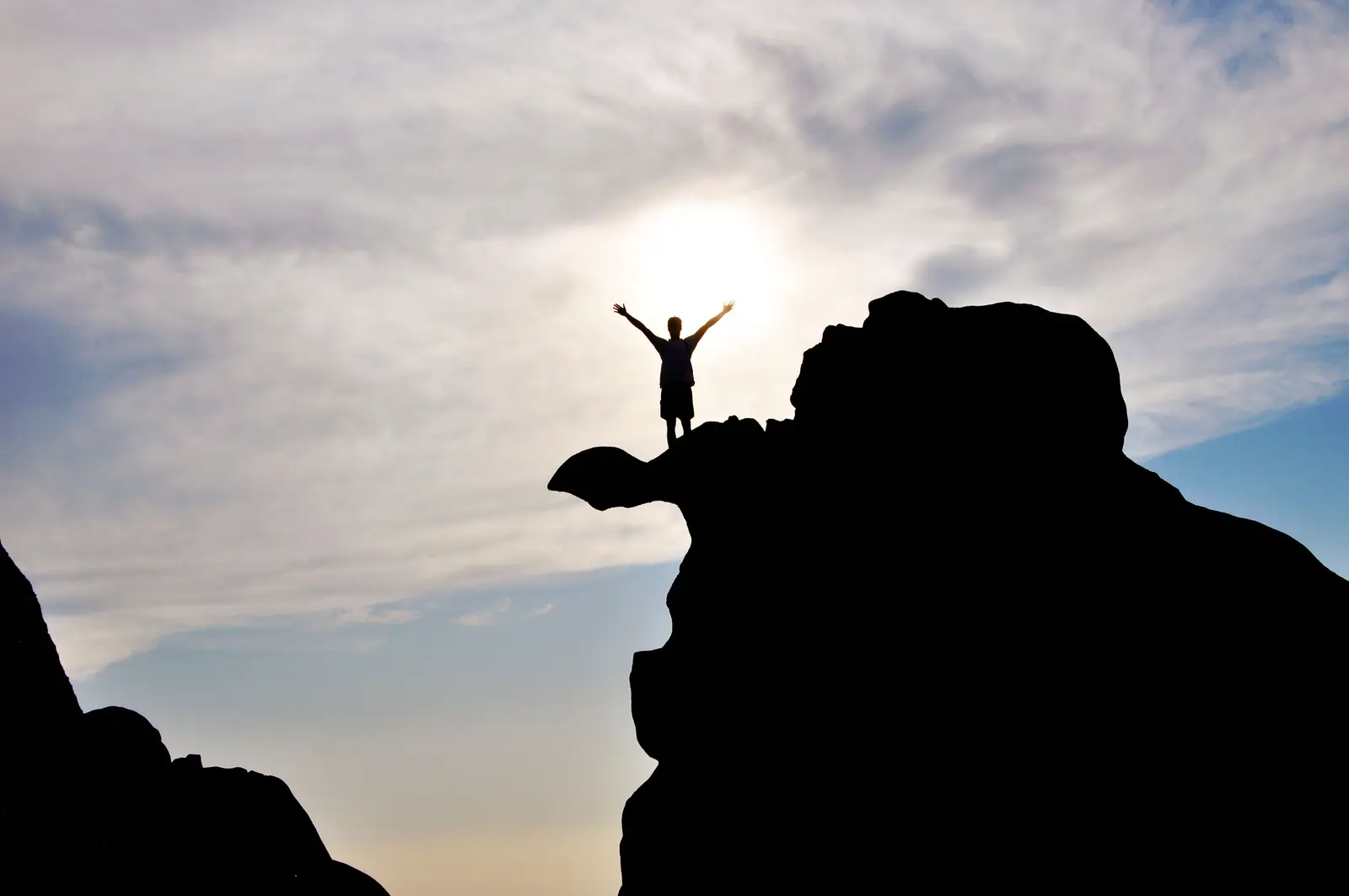 A man standing with arms raised on a rock ledge, one milestone down