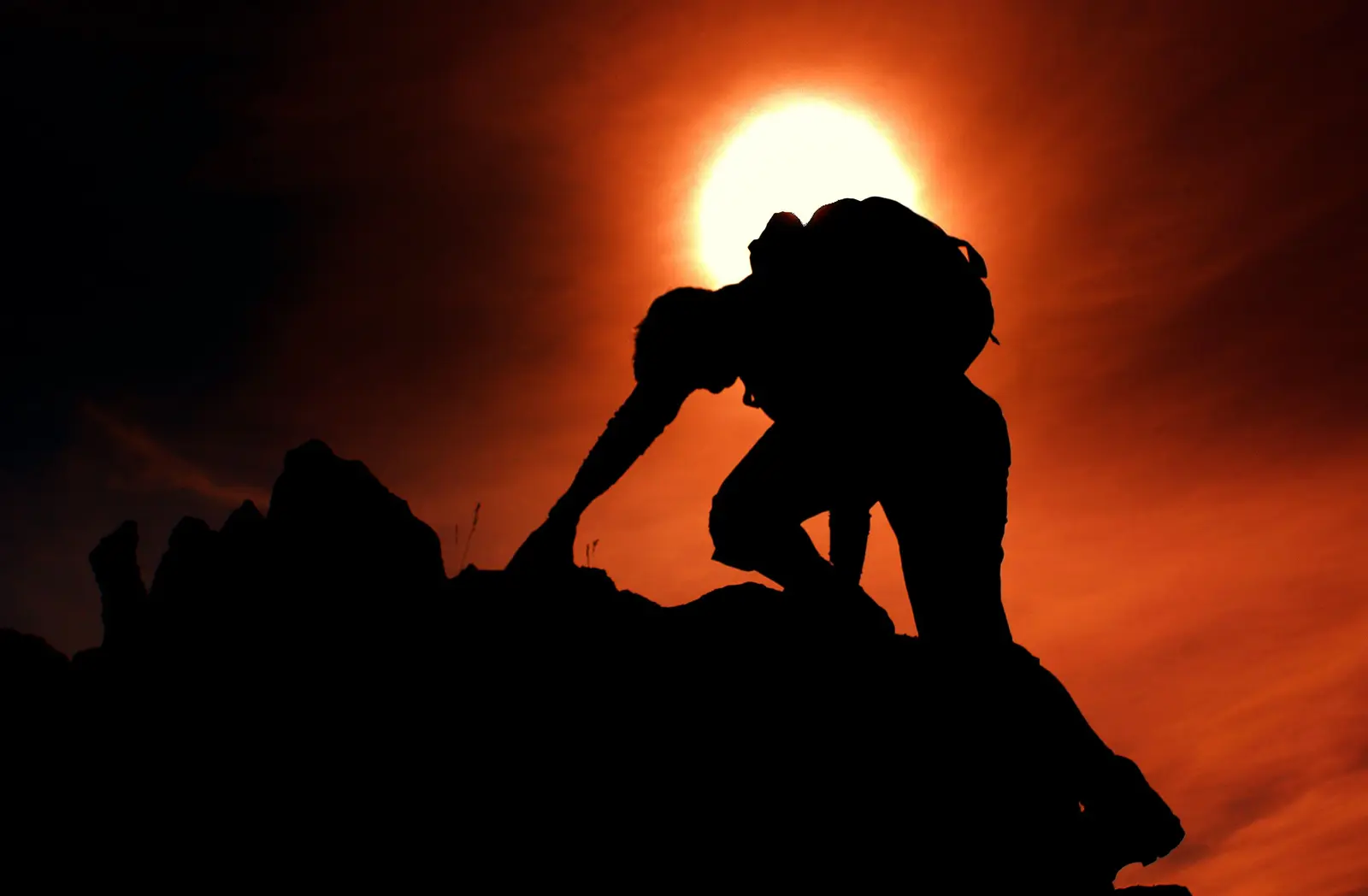 A man silhouetted at the top of a climb, sun rising behind him