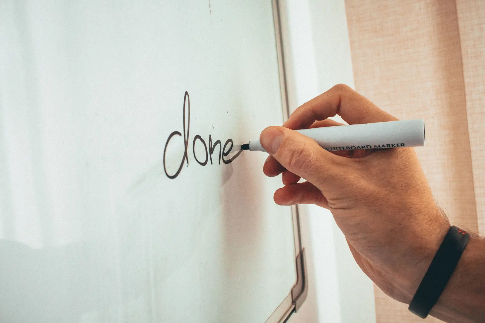 A hand writing 'done' on a whiteboard, another milestone checked off