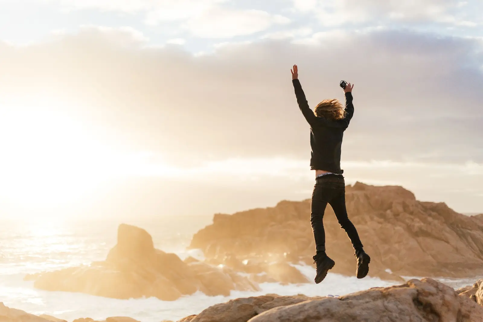 A man jumping along ocean rocks, full of energy