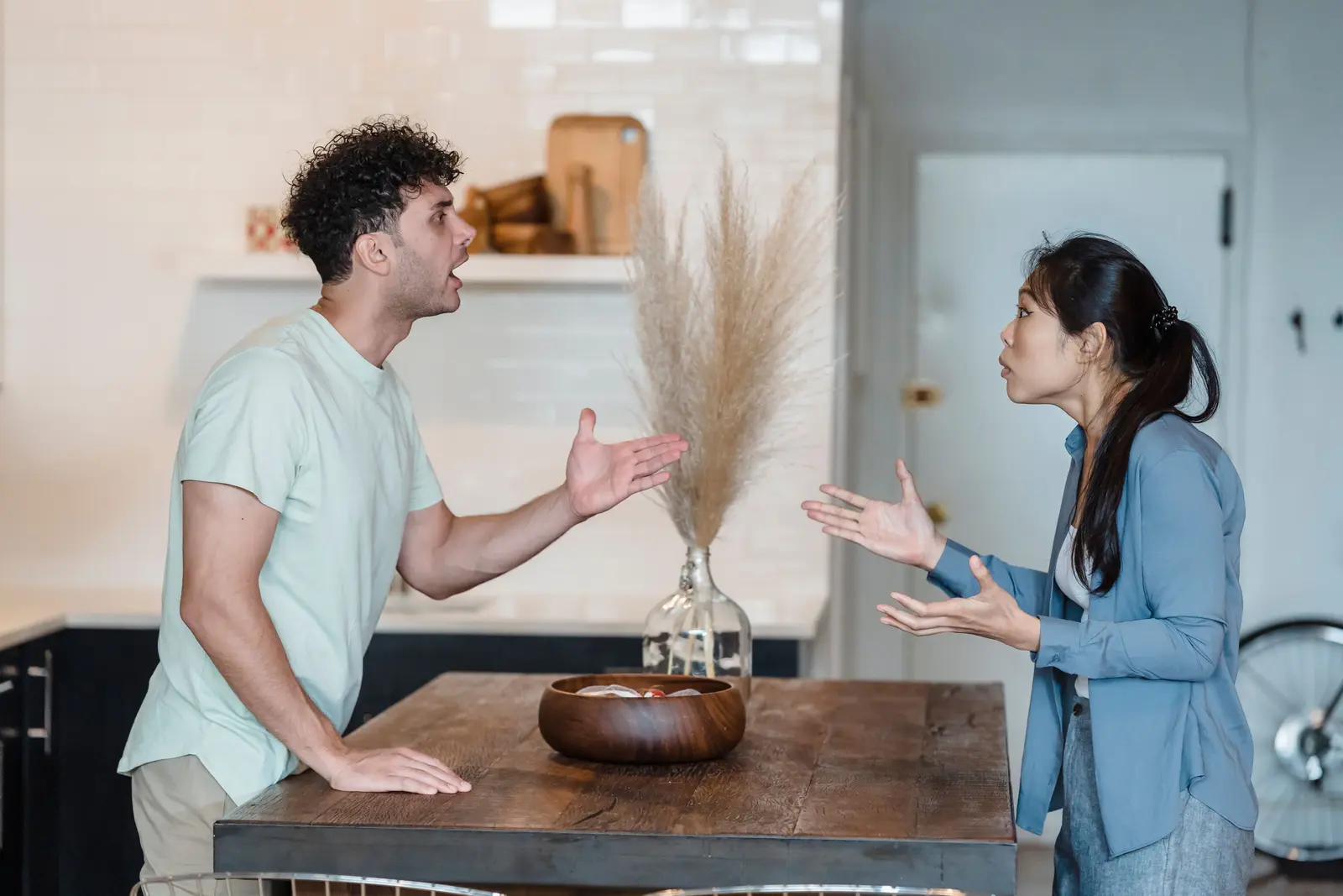 A man and woman arguing across a kitchen table