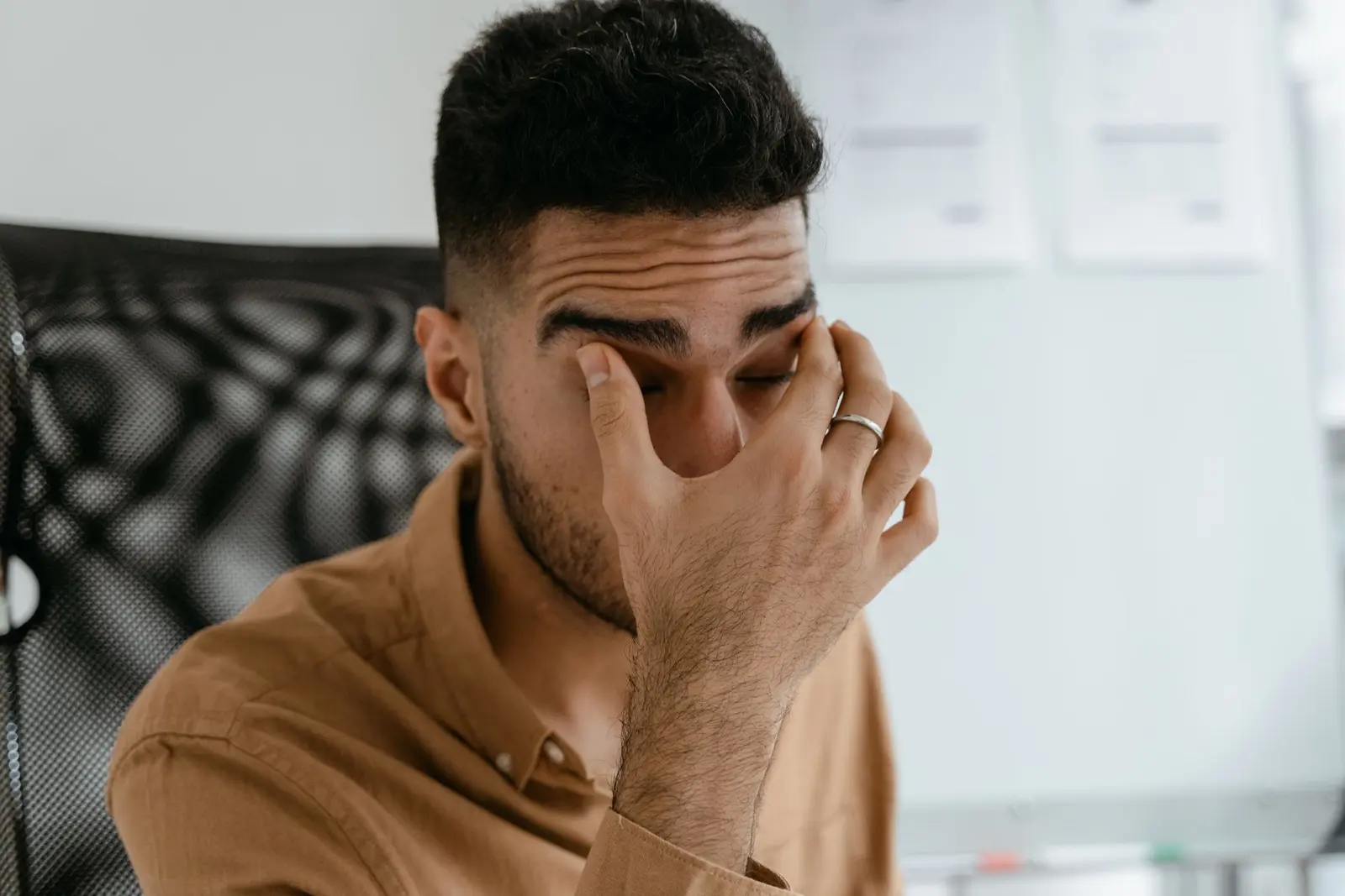 A man rubbing his eyes at his desk, worn down by stress