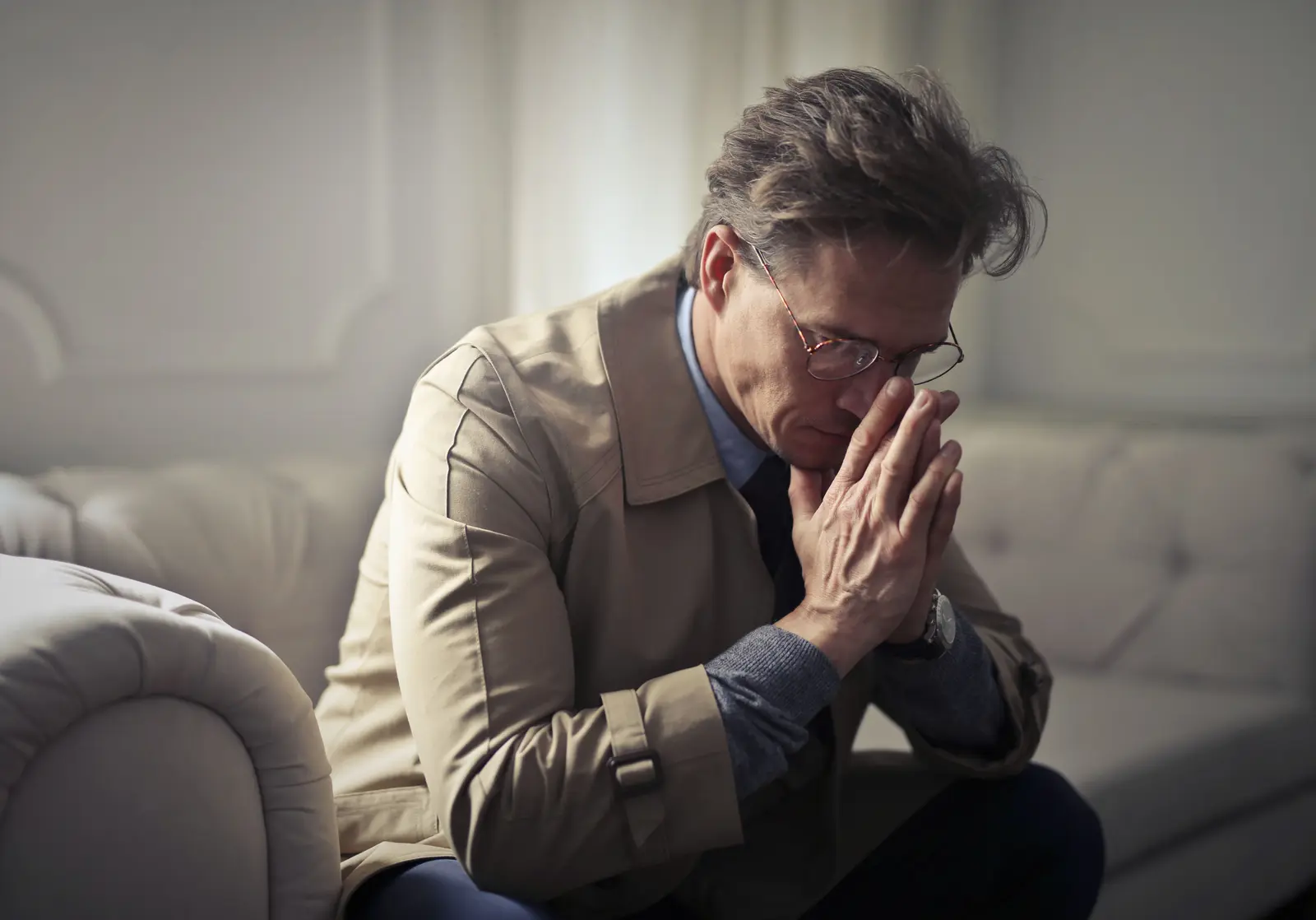 An older man sitting with his hands clasped, working through something heavy